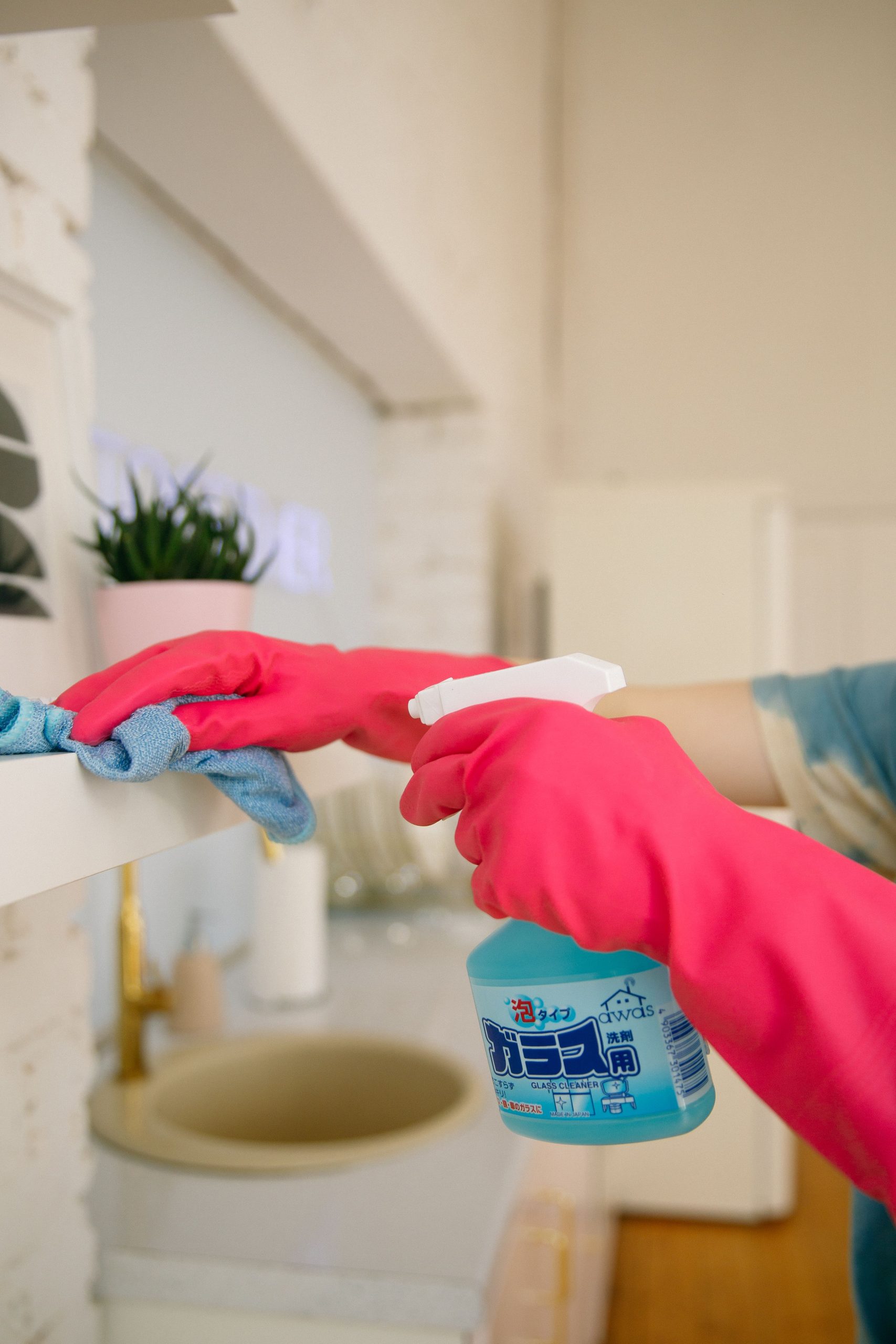 Person using spray bottle and cloth for cleaning a kitchen shelf, ensuring hygiene and cleanliness.